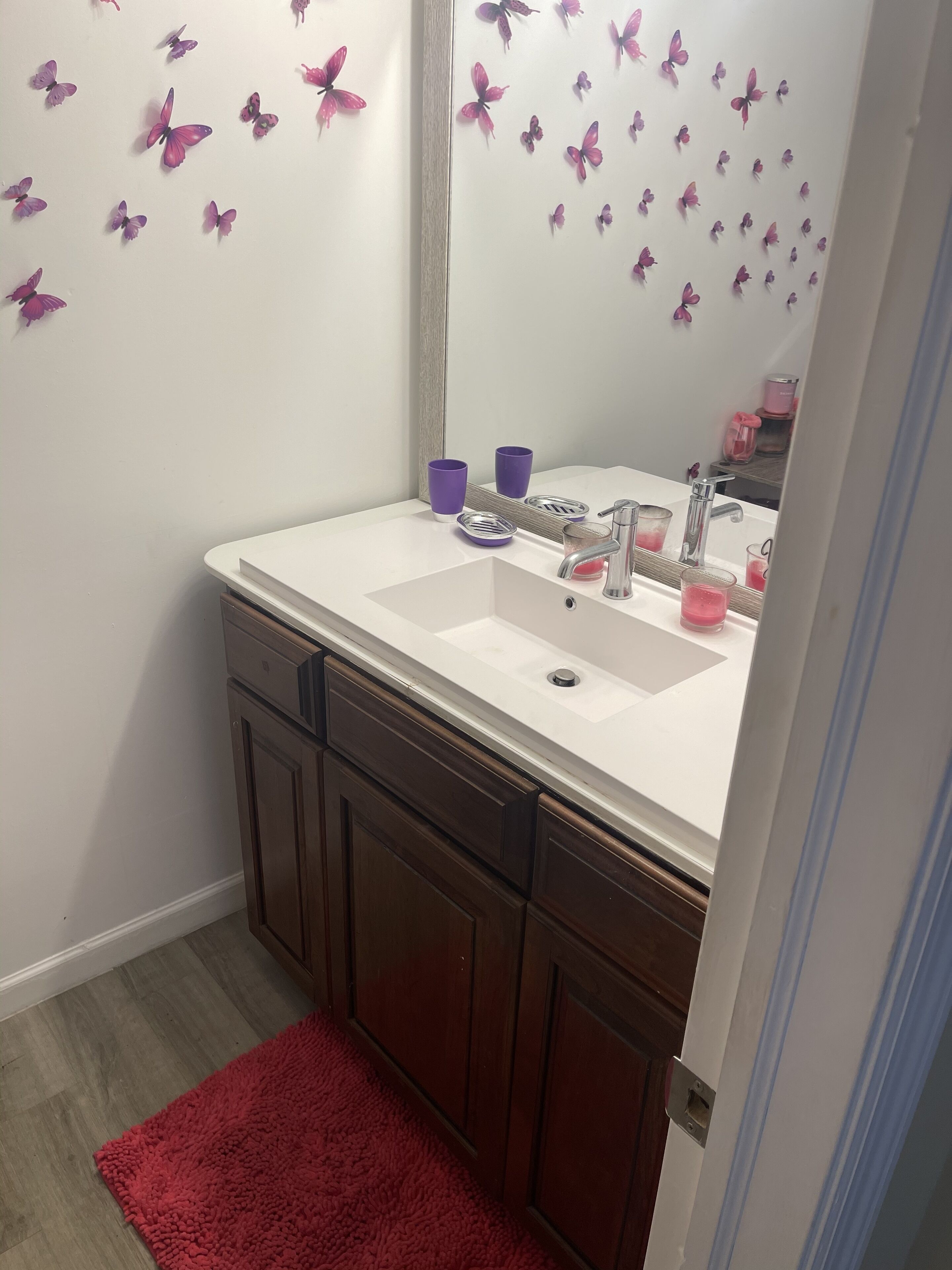 Un bagno con due lavandini, uno specchio, decorazioni a farfalla viola e un tappeto rosso.