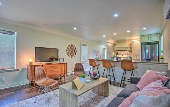 A modern living room with a TV, wooden furniture, and a kitchen area with a refrigerator. - 16 Mi to Disney: Cottage w/ Deck in Winter Garden (Winter Garden)