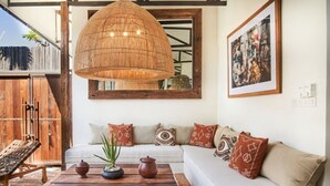 En hyggelig stue med en stor vævet loftlampe, en hvid sofa med mønstrede puder, et træbord med dekorative genstande og et stort spejl over sofaen.