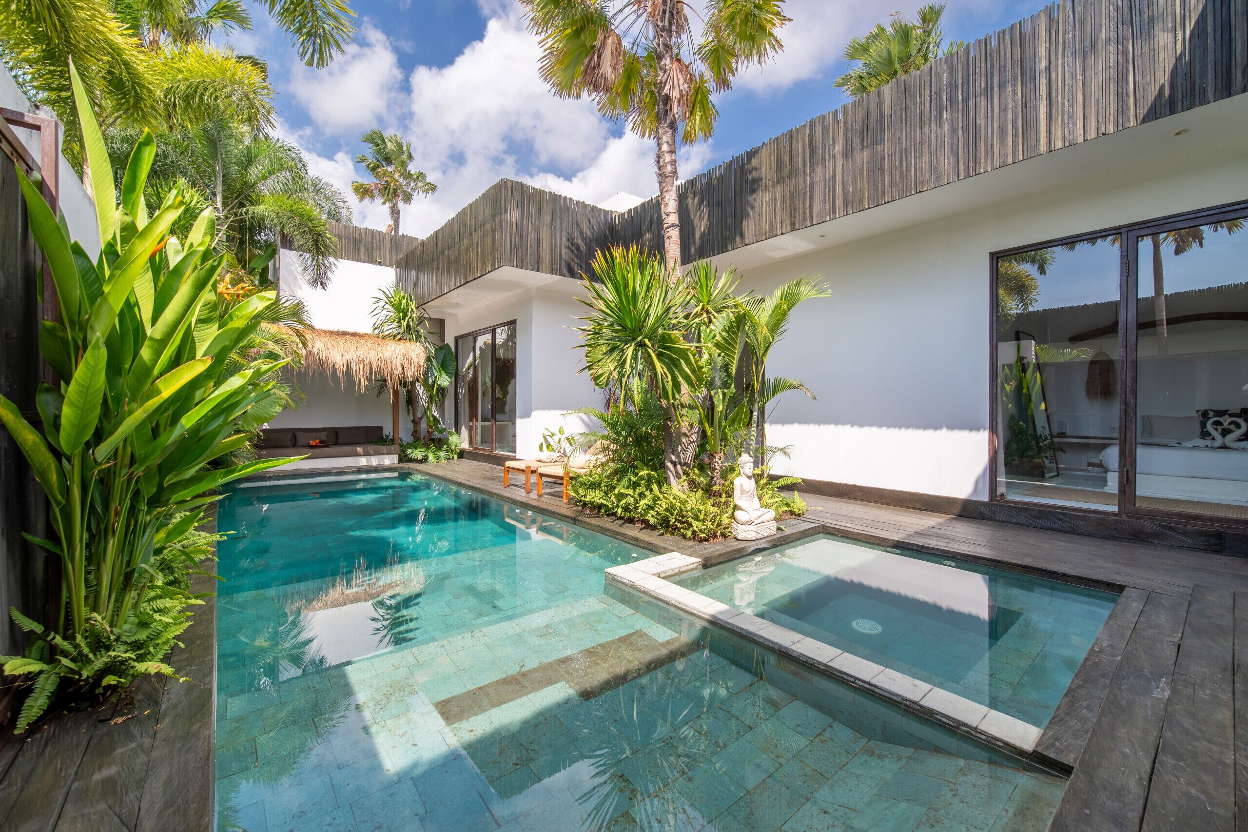 Zona de piscina moderna con una pileta cristalina, rodeada de plantas tropicales y una valla de madera.