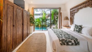 Ein Schlafzimmer mit einem großen Bett, einem Holzschrank, einem Deckenventilator und Blick auf ein Schwimmbad und Grünflächen.