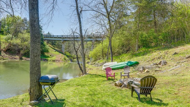 Eine Rasenfläche mit Grill, Stühlen und einem Kanu an einem Fluss.