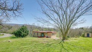 Ein kleines, eingeschossiges Haus mit rotem Dach und beige gefärbten Wänden, umgeben von einem grasbewachsenen Garten und Bäumen.