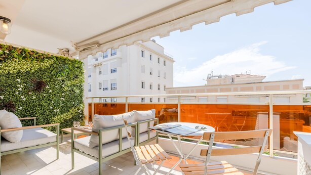 Une terrasse sur le toit agrémentée d’un mur végétal, de mobilier blanc et offrant une vue dégagée sur les bâtiments en arrière-plan.