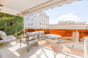 Une terrasse sur le toit agrémentée d’un mur végétal, de mobilier blanc et offrant une vue dégagée sur les bâtiments en arrière-plan.