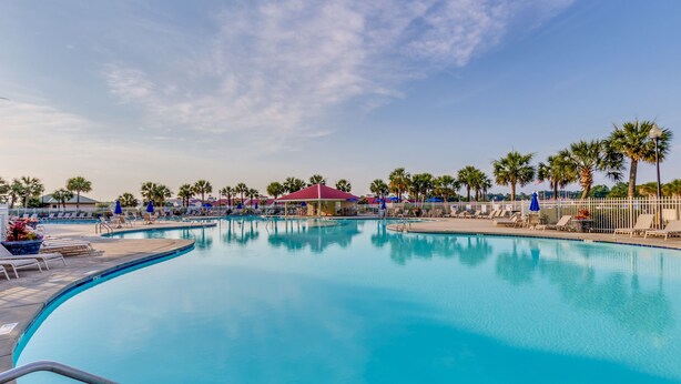 A swimming pool with lounge chairs and umbrellas, surrounded by palm trees and a clear sky. - Enjoy Tranquility at Barefoot Resort & Yacht Club 7th Floor Waterfront Unit (North Myrtle Beach)