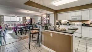 A modern kitchen with white cabinets, a central island, and a dining area with a table and chairs. - Enjoy Tranquility at Barefoot Resort & Yacht Club 7th Floor Waterfront Unit (North Myrtle Beach)