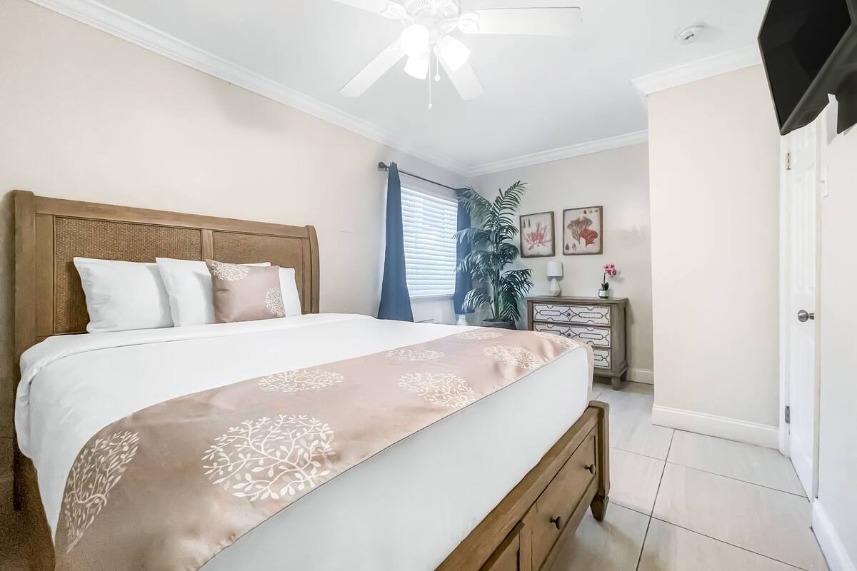 A bedroom with a bed, a ceiling fan, a dresser, and a door.