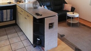 Un espacio habitable compacto con área de cocina, un sofá de cuero negro, una mesita auxiliar y una chimenea integrada.