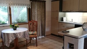Una cocina con mesa, sillas, horno empotrado y una ventana con cortinas.