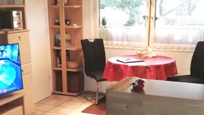 Un espacio habitable compacto con kitchenette, una zona de comedor con una mesa roja y un televisor en la esquina.