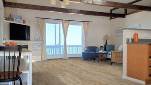 Amplia sala de estar con piso de madera, una mesa de comedor con sillas, un sofá azul y un televisor sobre un soporte blanco.