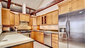 Una cocina con armarios de madera, un refrigerador de acero inoxidable, horno empotrado y protector de encimera de piedra.