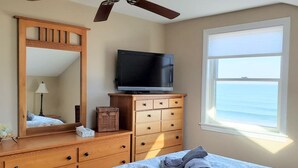Un dormitorio con cama, cómoda, televisor, espejo y ventana con vista al océano.