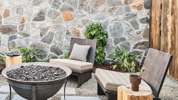 A stone wall, outdoor seating with cushions, a metal fire pit, and potted plants.