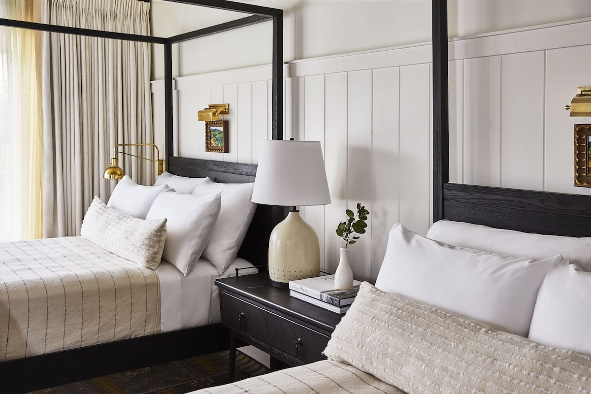 A four-poster bed with white linens, a bedside table with a lamp, and a framed picture on the wall.