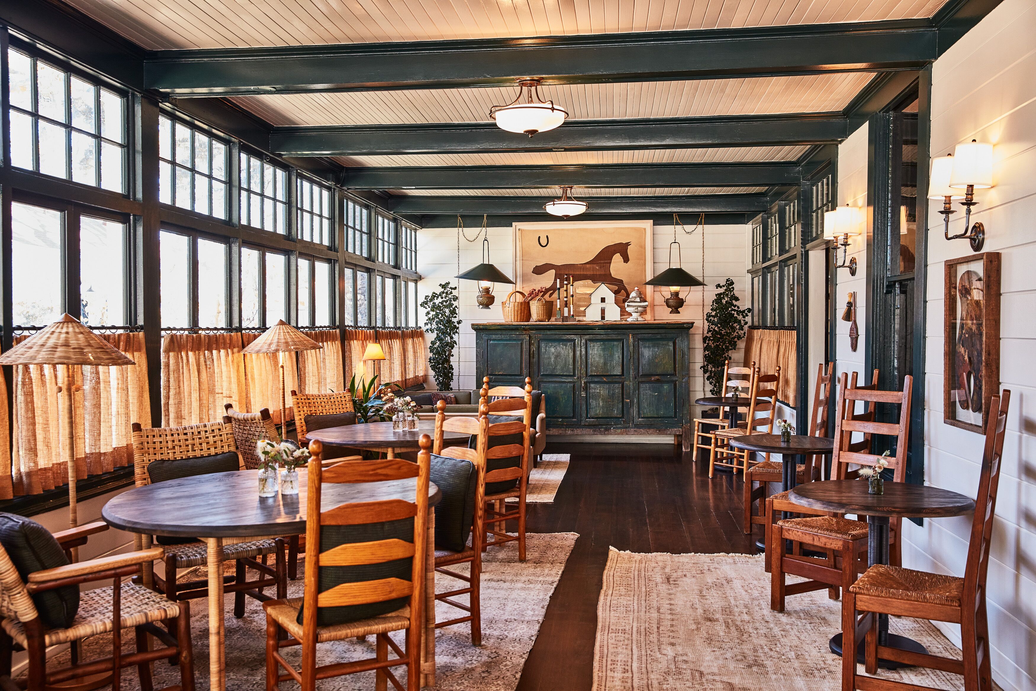 A spacious dining area with wooden tables and chairs, large windows, and a rustic decor.