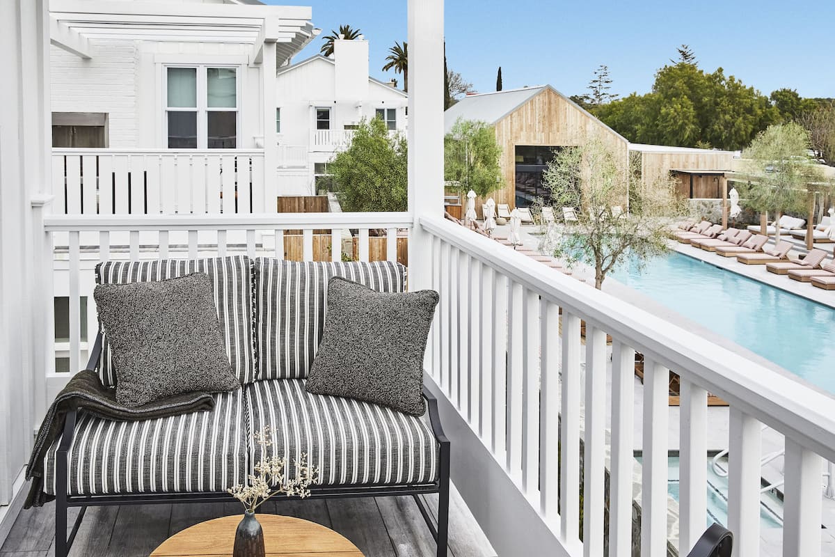 A balcony with a striped sofa, a pool, and a wooden deck.