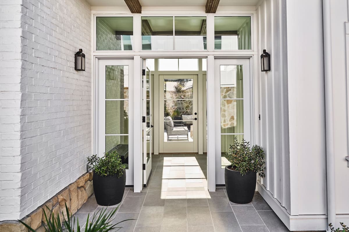 A modern house entrance with a double door, potted plants, and a stone wall.