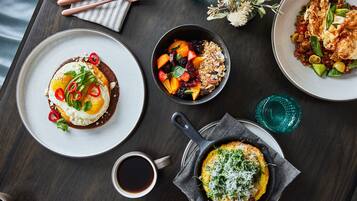 A dining table with various dishes, including a plate with a fried egg, a bowl of fruit salad, and a skillet with a baked dish.
