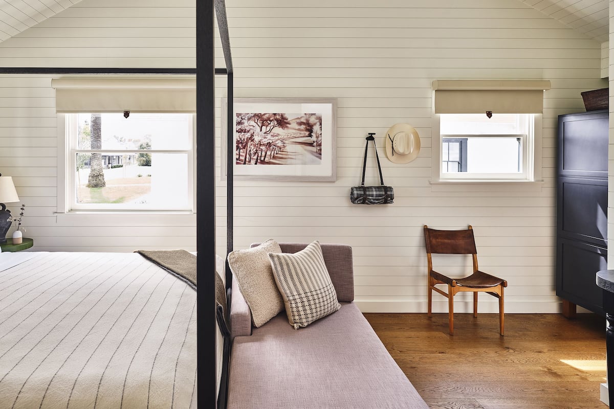 A bedroom with a four-poster bed, a sofa, a chair, and a painting on the wall.