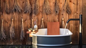 A bathtub with a wooden side panel, a black faucet, and a wooden tray with a small plant.