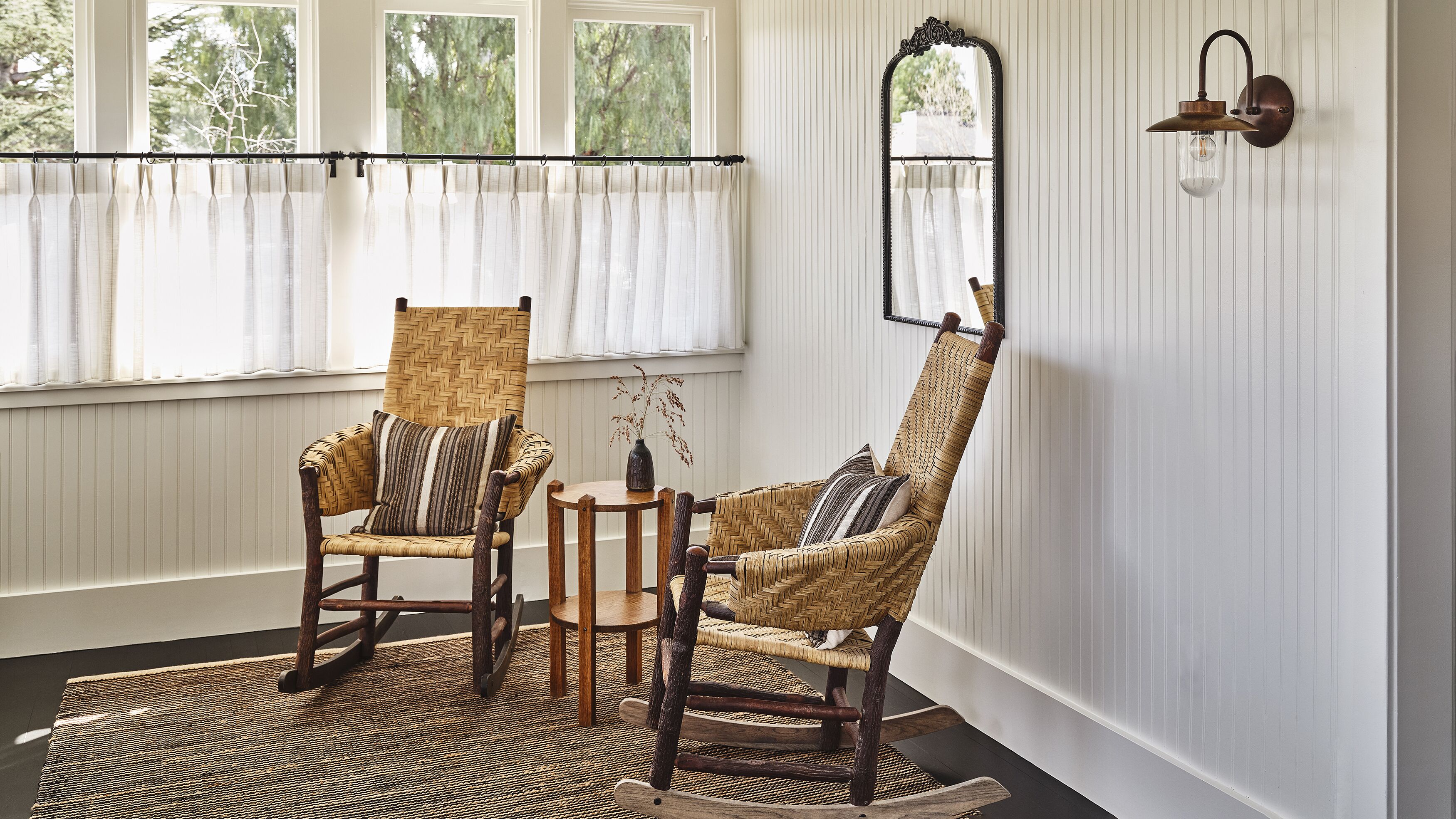A room with two wicker chairs, a small round table, and a mirror on the wall.