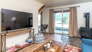 Un salon doté d’un téléviseur à écran plat, d’une table basse en bois, d’un canapé, d’une cheminée en pierre et d’une grande fenêtre avec des rideaux.