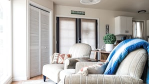 Un salon chaleureux avec un canapé, une table basse et une plante décorative. On y trouve une porte coulissante surmontée d’une enseigne, ainsi qu’un meuble en arrière-plan.