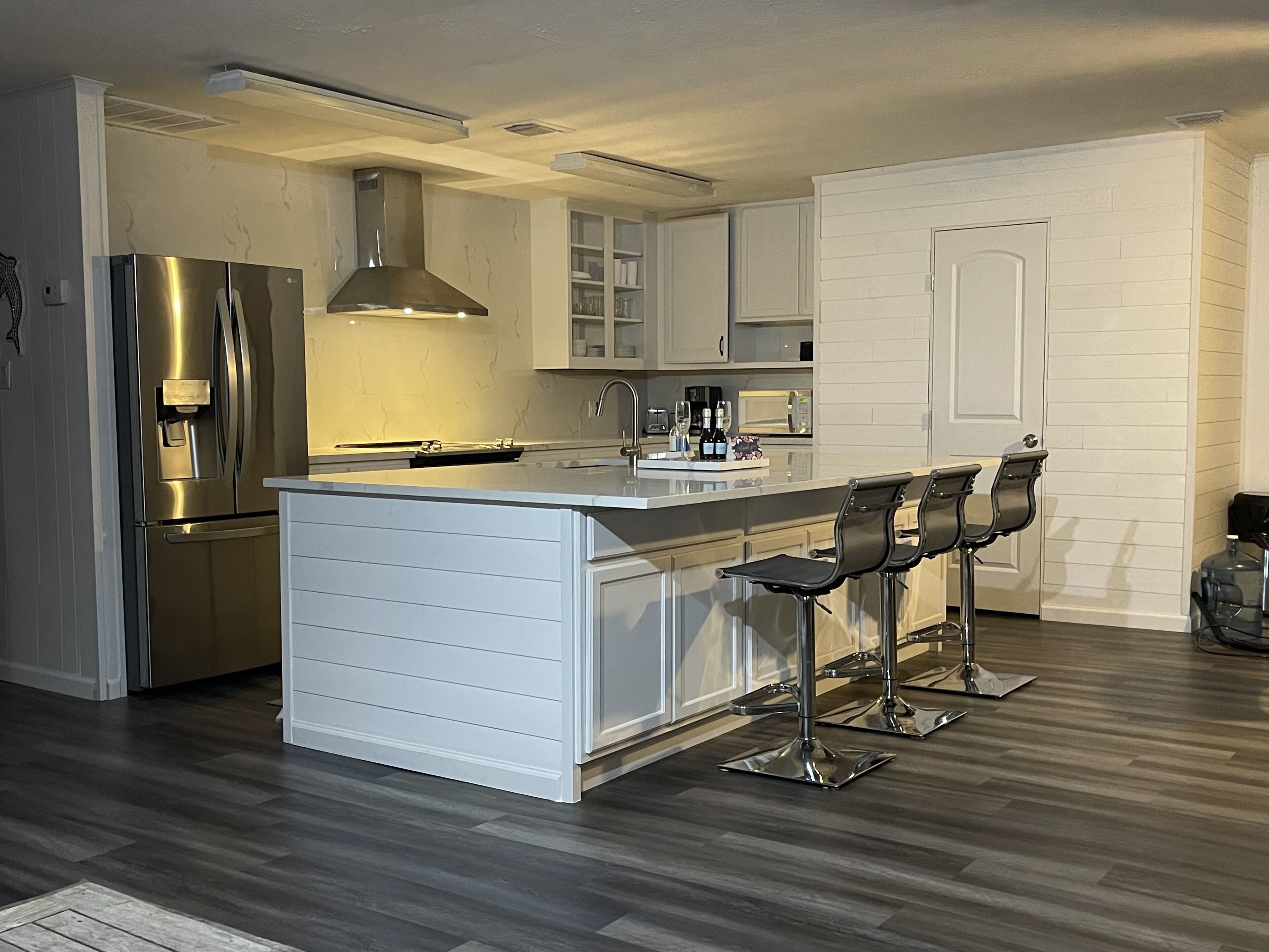 Een moderne keuken met een roestvrijstalen koelkast, een centraal eiland met barkrukken en witte keukenkastjes.