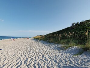A sandy beach with a clear sky, a grassy hill, and a few people in the distance.