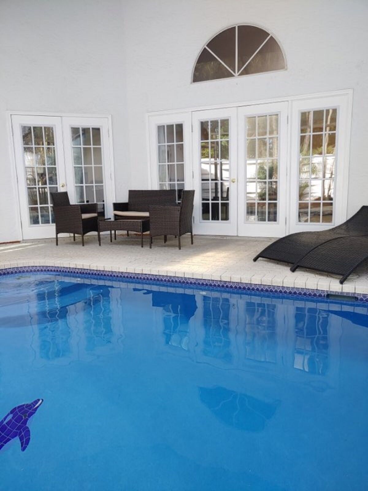 An indoor swimming pool with a tiled edge, a dolphin decoration, and a seating area with chairs and a table.