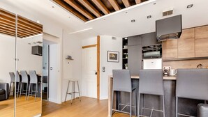 A modern kitchen with a wooden ceiling, a bar area with grey chairs, and a dining table. - High standing apartment near Porte de Versailles (Vanves)