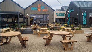 An outdoor seating area with wooden tables and chairs, a building with signs for 'Drink Relax Dance' and 'RECEPTION', and a 'Welcome' sign. - St Osyth- Sleeps8-freeparking-wifi-holidaypark (Clacton-on-Sea)