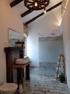 A modern bathroom with a wooden vanity, a large mirror, a freestanding toilet, and a shower area with a glass door. - Beautiful 3-Bed House in Kotli (Kotli)