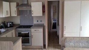 Eine kleine Küche mit Herd, Backofen und Schränken, die in einen Essbereich mit Tisch und Stühlen übergeht.