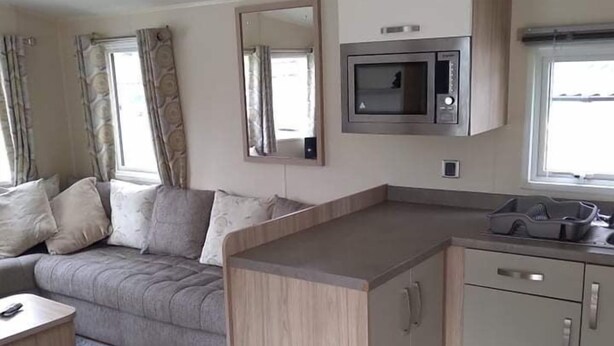 Ein kompakter Wohnraum mit Sofa, einem kleinen Esstisch, einer Küchenzeile mit Mikrowelle und einem Schrank.