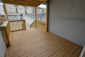 Une terrasse en bois avec des garde-corps, une vue sur les maisons voisines et un mur en métal ondulé.