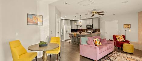 A modern living room with a dining area, a kitchen in the background, and a ceiling fan.