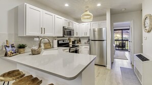 A modern kitchen with white cabinets, stainless steel appliances, and a central island. There is a view of a balcony through an open door.
