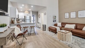 A modern living room with a brown leather sofa, a wooden coffee table, and a dining area with a white table and chairs.