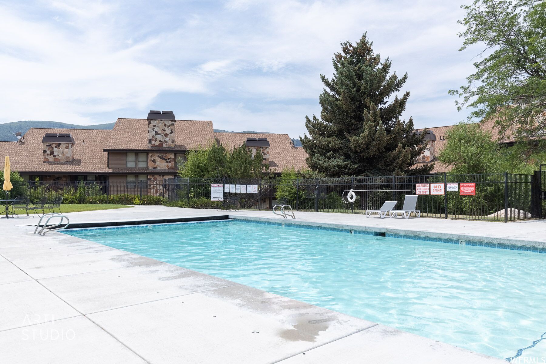 A swimming pool with a clear blue water, surrounded by a paved deck. There are lounge chairs and a lifeguard stand.