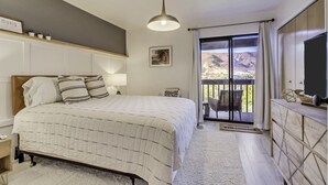 A bedroom with a bed, bedside table, lamp, and a view of the outdoors through a sliding door.