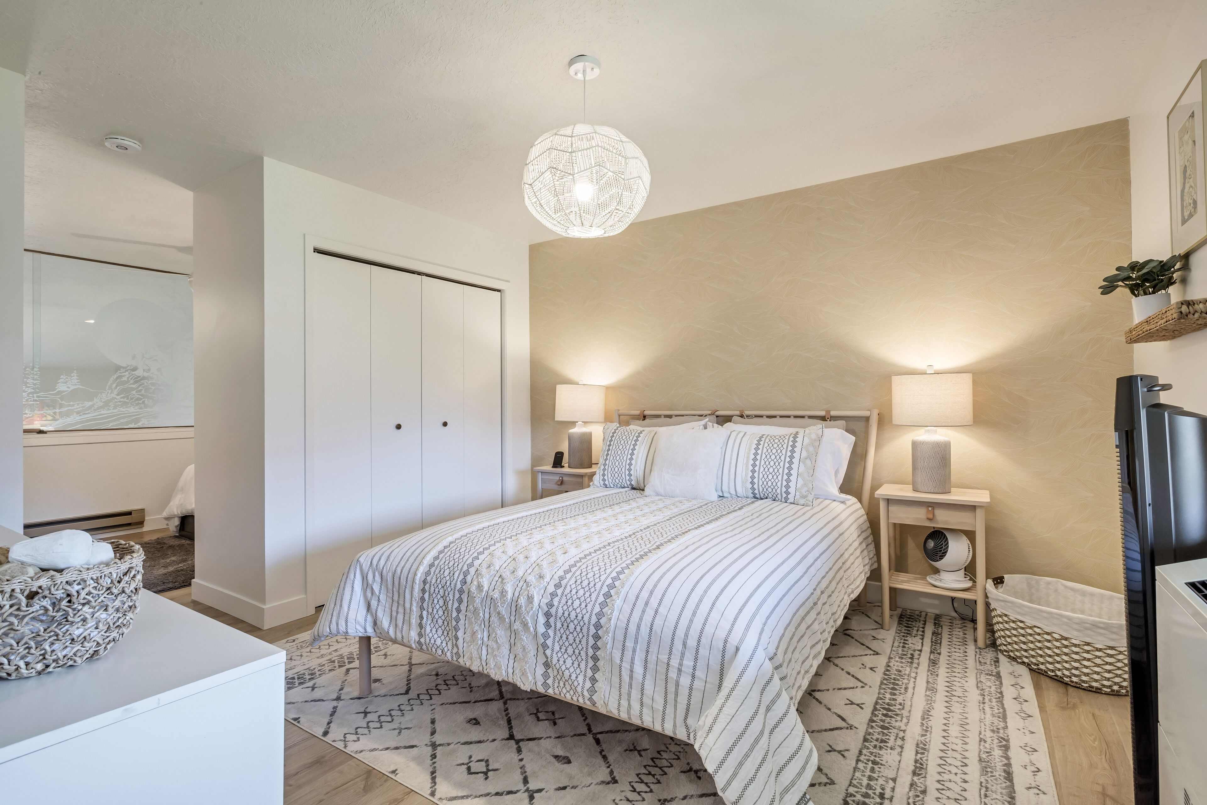 A bedroom with a bed, bedside lamps, a TV, and a decorative wall hanging.