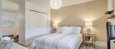 A bedroom with a bed, bedside lamps, a TV, and a decorative wall hanging.