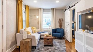 A compact living space with a sofa, a blue armchair, a small coffee table, and a TV on a cabinet.