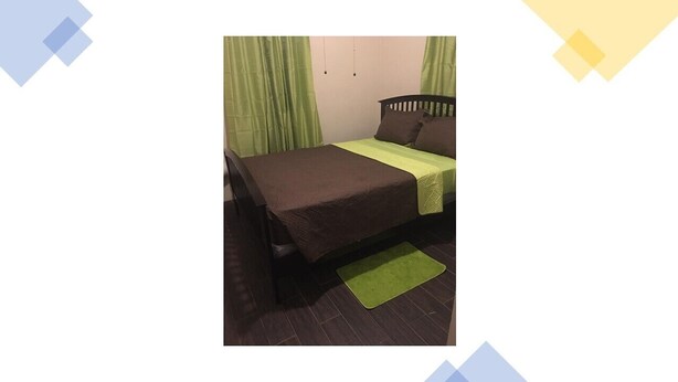 A single bed with a brown bedspread and a green throw pillow, a green rug, and a wooden headboard. - Veronica's Villa (St Thomas)