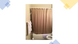 A bathroom with a beige shower curtain, a white towel rack with a towel, and a toilet with a purple toilet paper holder. - Veronica's Villa (St Thomas)