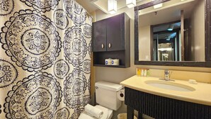 A bathroom with a patterned shower curtain, a toilet, a sink with toiletries, and a mirror above the sink.