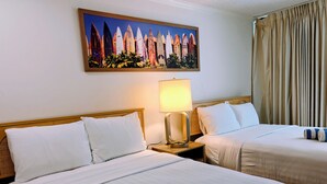 A hotel room with two beds, a nightstand with a lamp, and a painting of surfboards on the wall.